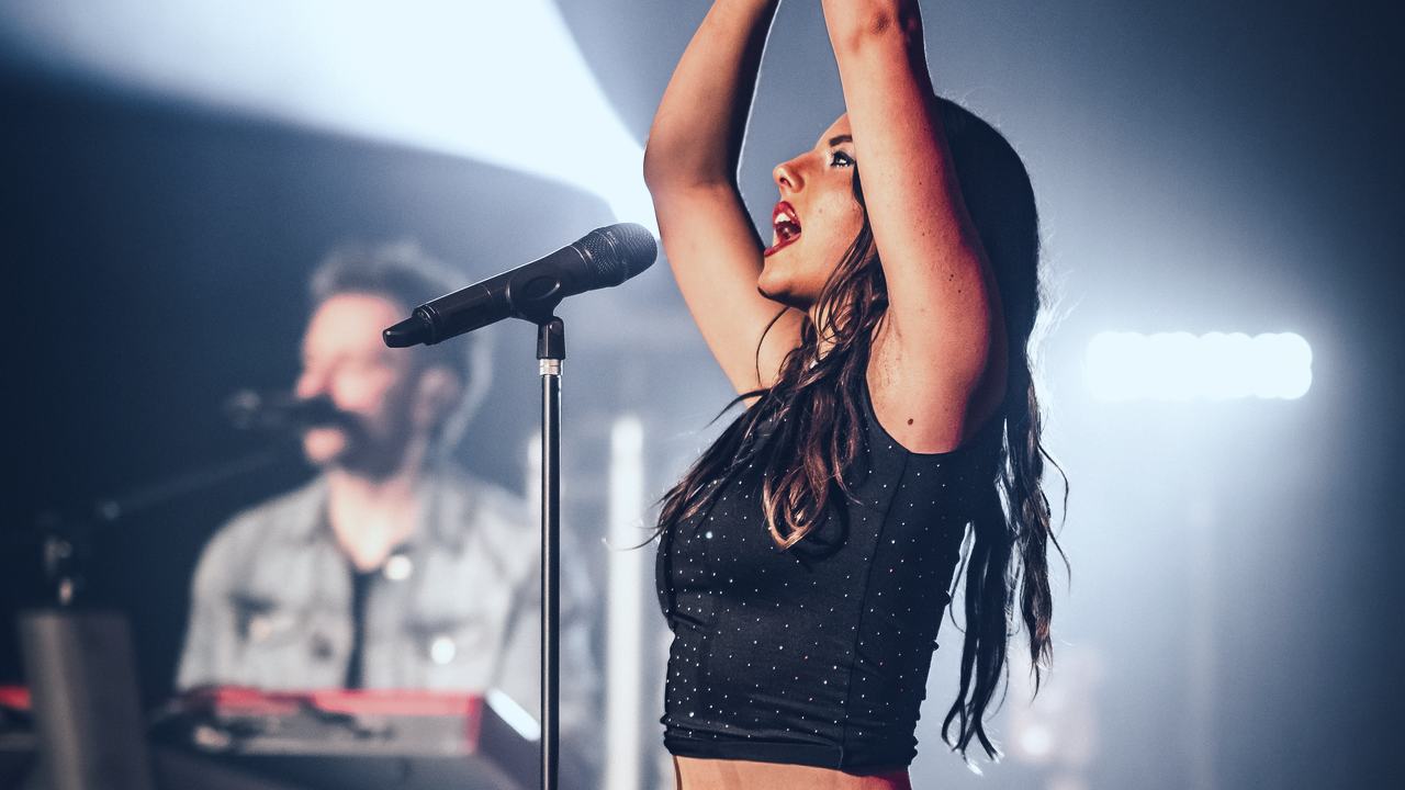 The Dua Lipa Experience's singer with her arms raised on stage
